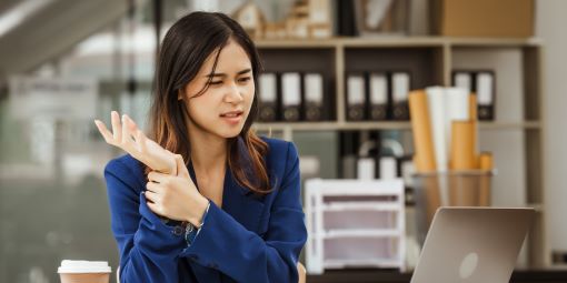 A woman sitting at her office desk has wrist pain.