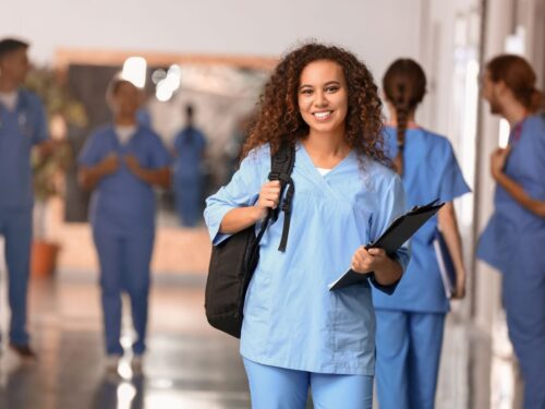 A female nurse with backpack and clipboard stands in front of her colleagues.