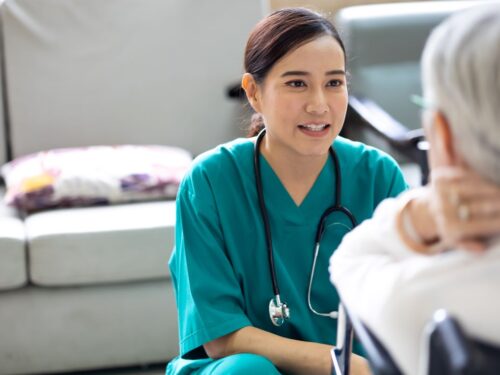 A female nurse speaks to an elderly woman with a sore neck.