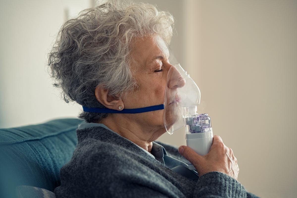 An elderly woman uses a nebulizer.