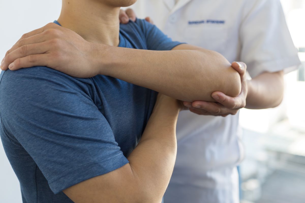 A physiotherapist treats a man's shoulder.