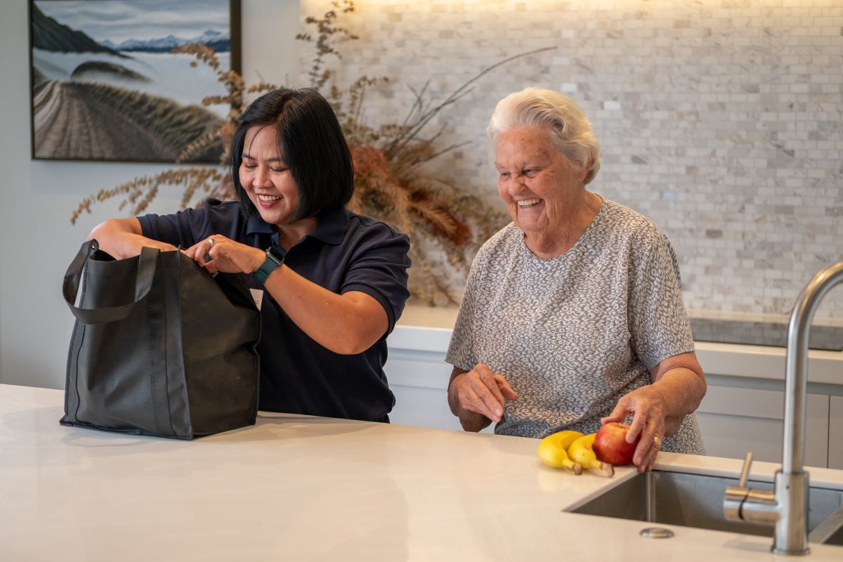 A carer helps an elderly woman with her groceries.